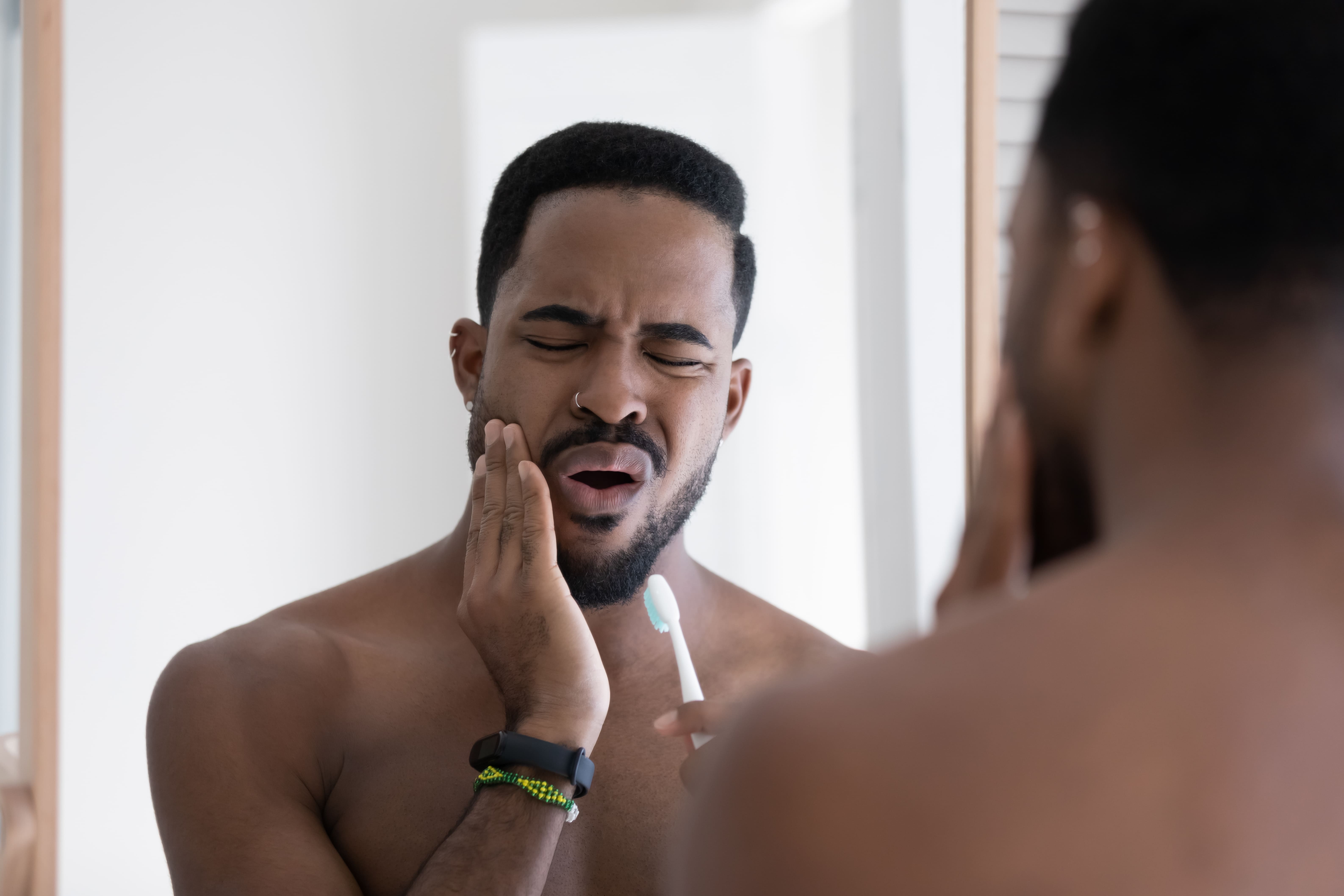 Man holds his jaw from gum pain after brushing his teeth too hard.